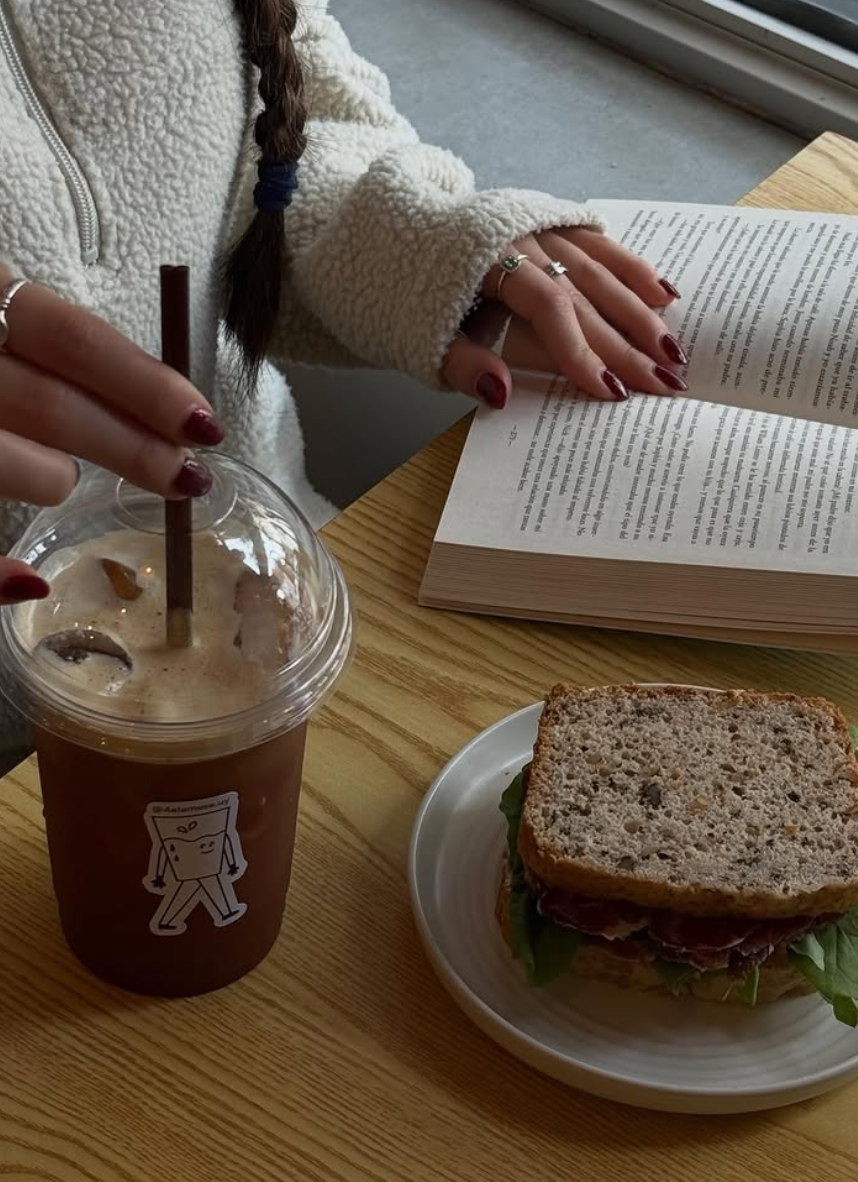 Cliente leyendo con un cold brew y un sándwich en la ventana del local